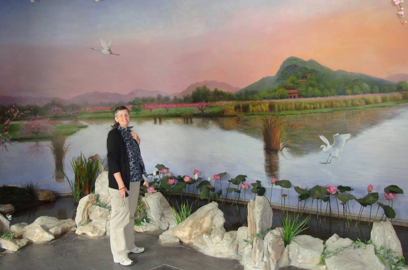 Picture:  Ruth stands in front of a huge mural depicting the orchards of Yang Shan.  The Tao Bo Yuan (Peach Museum), Yang Shan, Wuxi, China